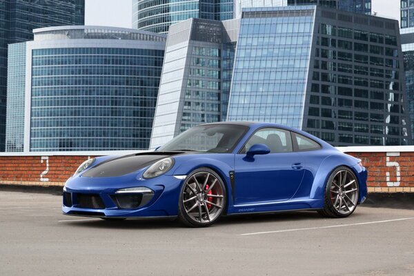 A blue Porshe Carrera 911 Stinger stands on the top floor of a multi-level parking lot facing the lens