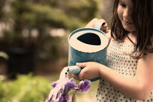 A girl waters flowers from a blue watering can