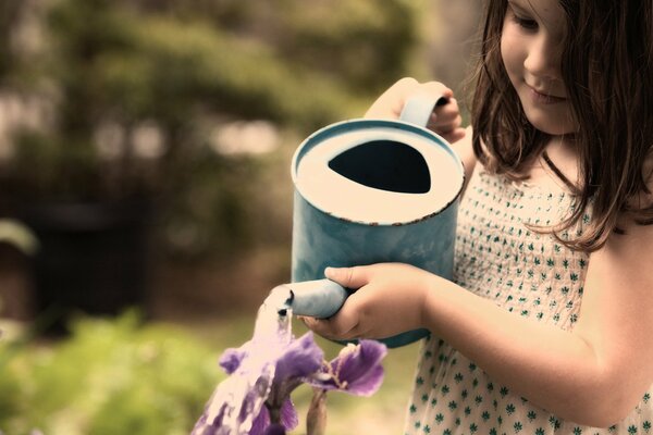 Dziewczyna podlewa kwiaty z niebieskiej konewki