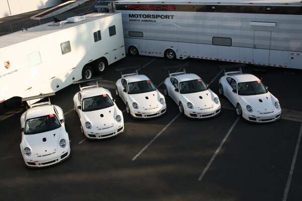 Mehrere weiße Autos der Marke porsche 911 gt3 vor dem Hintergrund von Lieferwagen