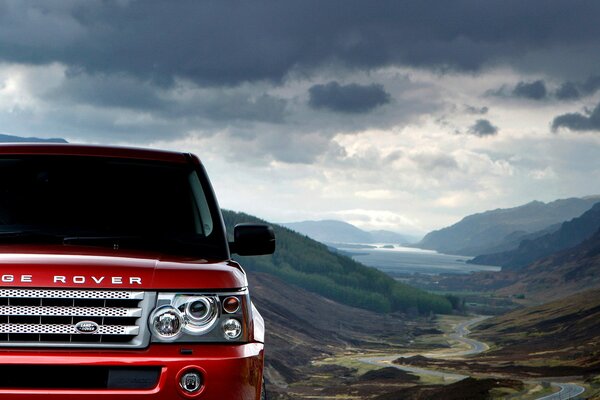 Red range rover sport car under black clouds of mountain terrain