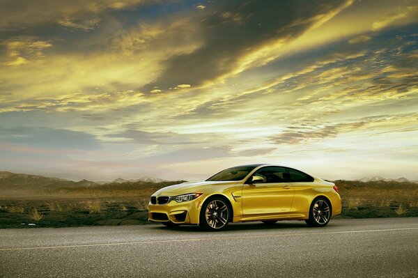 A golden BMW M4 car stands against the backdrop of a beautiful sunset