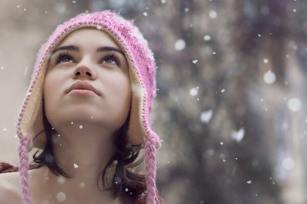 Sguardo sorpreso della modella in un cappello che vede i fiocchi di neve