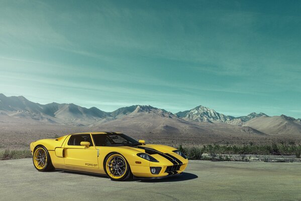 Yellow with two black stripes, along the surface of the body, Ford GT stands against the background of mountains