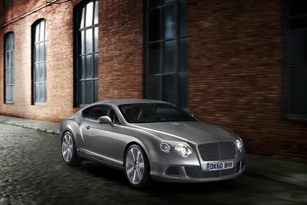 Серый автомобиль Bentley Continental стоит рядом с кирпичным заводом