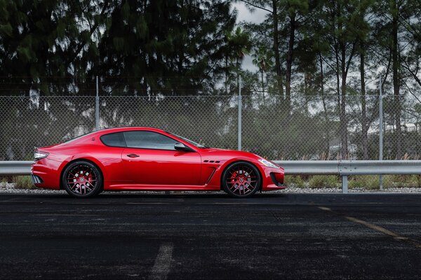 Un coche rojo de la marca Maserati se encuentra en una pista de carreras cercada