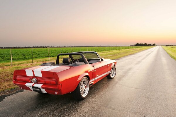 Ford Mustang rojo con rayas en el cielo y la carretera con el campo