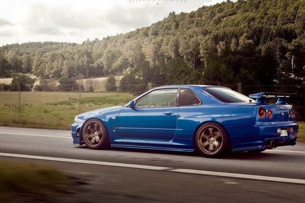 A blue Nissan is racing down the road behind the trees