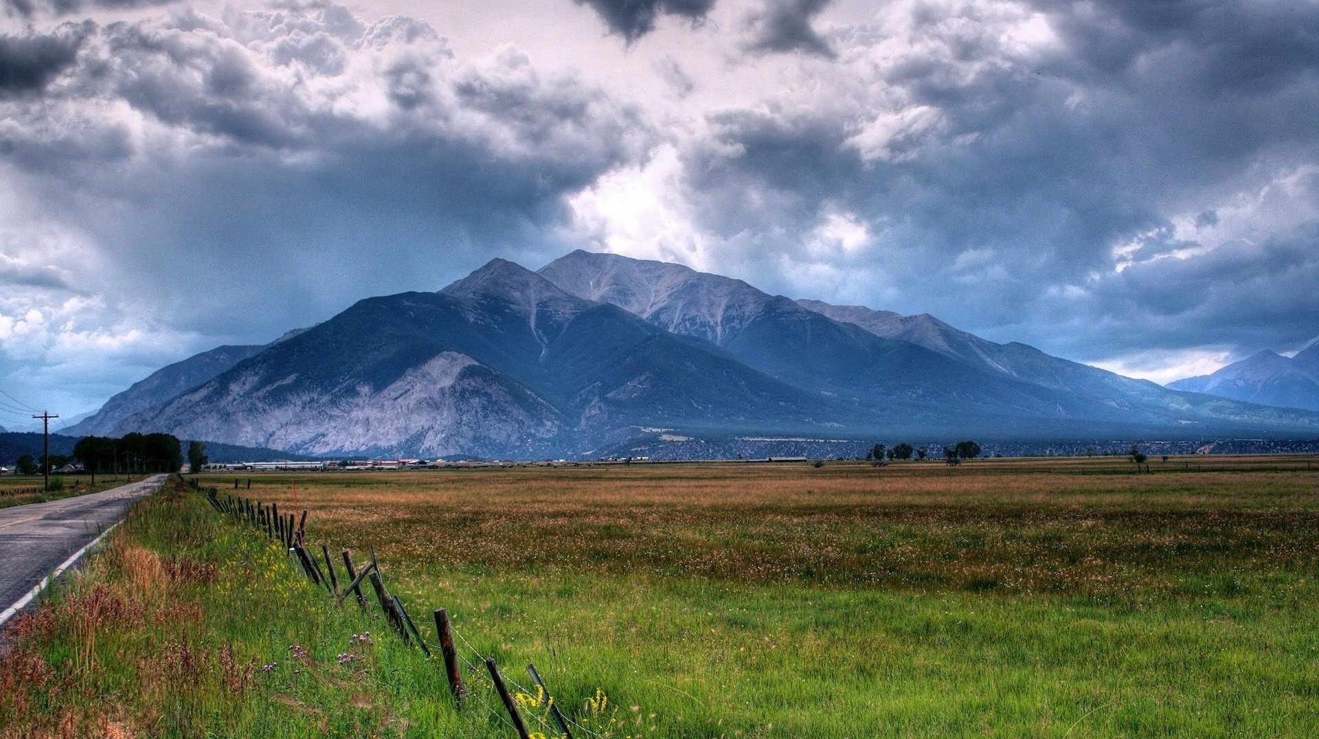 berge weit weg von der stadt straße straßenrand gras himmel wolken horizont zaun