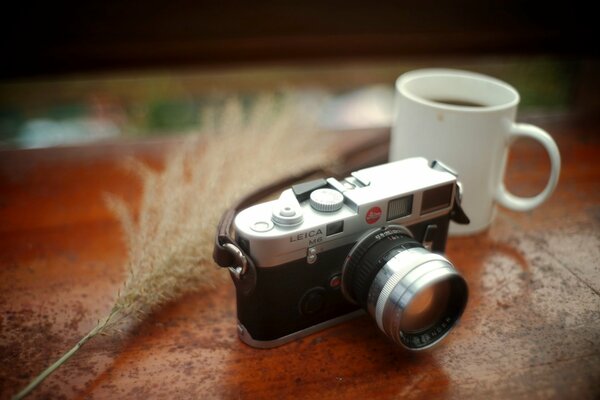 Black and silver Leica camera with a tie on the table with a cup of coffee