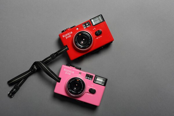 Two cameras pink and red with ties on a gray background
