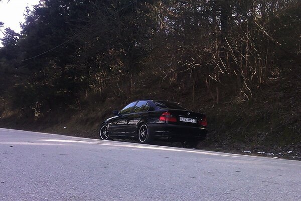 Black car on the road against the background of the forest