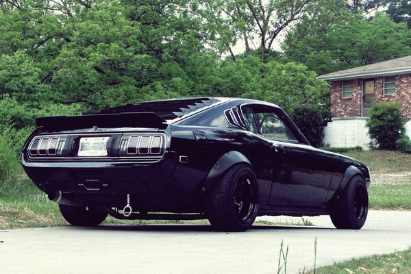 Un Mustang negro se detiene en el estacionamiento al lado de la casa