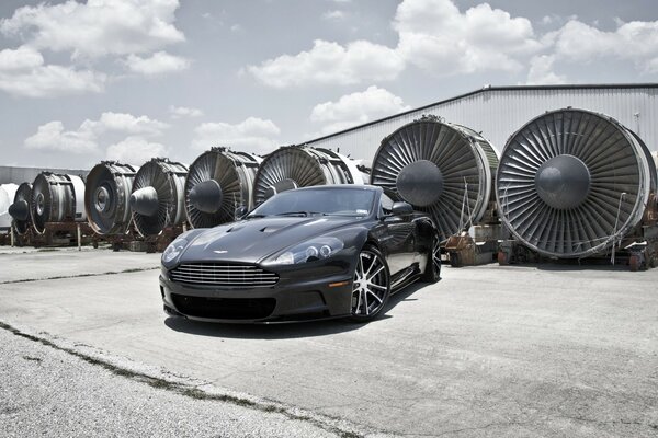 Black Aston Martin on the background of aircraft turbines