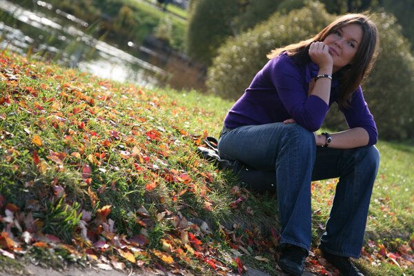 Mädchen sitzt auf dem Rasen mit Herbstlaub