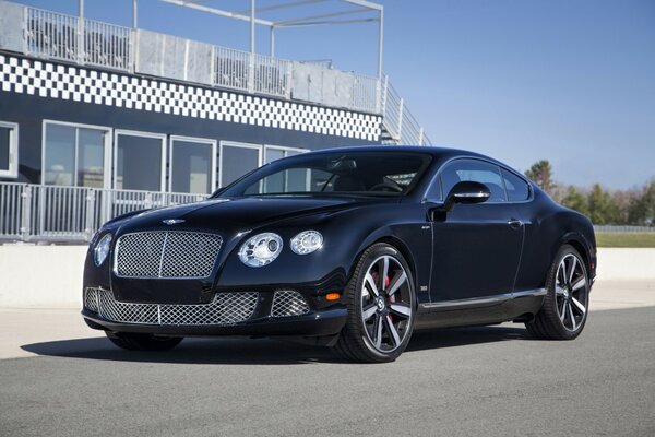 A black 2013 Bentley on the street next to the building