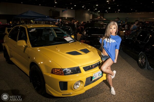 A girl in a blue T-shirt at a yellow car