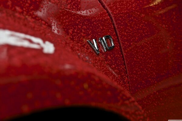 The wing of a red car covered with water droplets