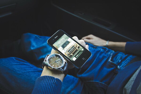 A hand with a watch and a phone is lying on his legs in jeans