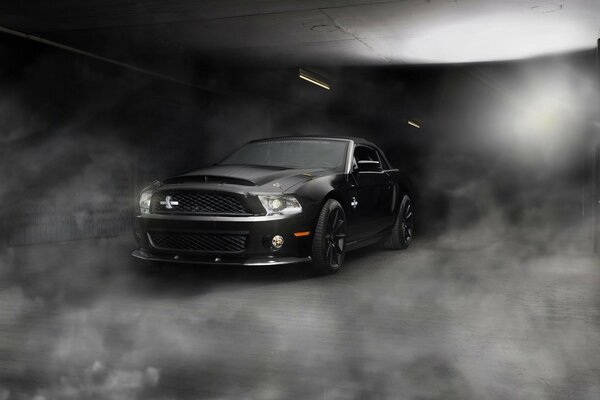 A black Ford Mustang car cleaves the road in the fog