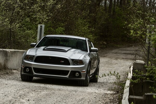 Un automóvil Mustang plateado viaja a lo largo de una carretera fuera de la ciudad