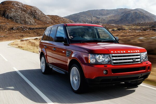 Coche rojo Renge Rover en la carretera en el fondo de las montañas