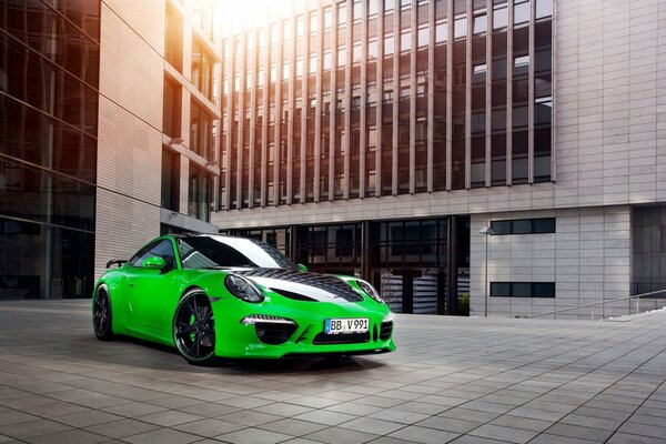 Green Porsche with black inserts on the background of a modern building in the sunlight