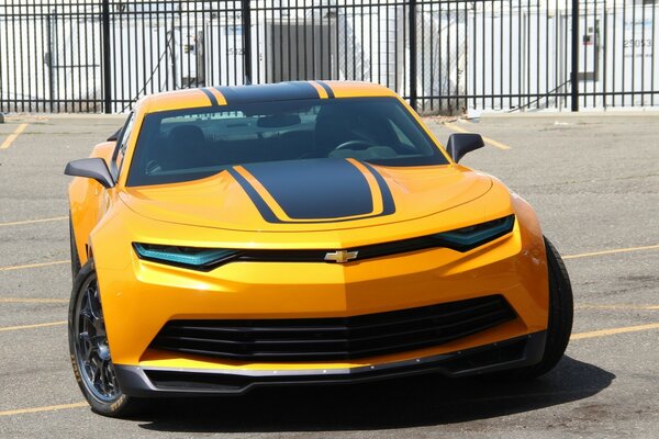 Горячий сладкий Chevrolet Camaro на солнечной улице на фоне забора