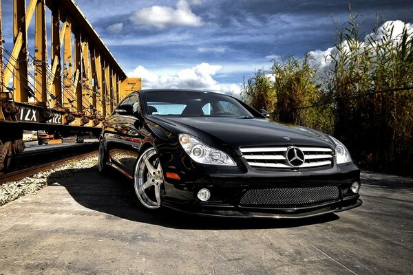Mercedes Benz czarny stoi przed wagonami kolejowymi