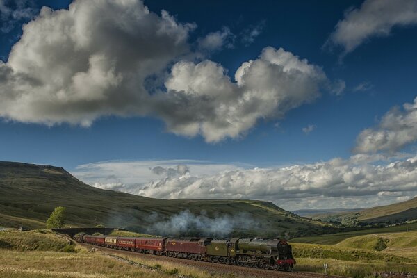 Train with a steam locomotive on a beautiful terrain with clouds