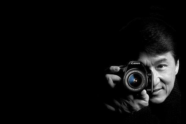 Jackie Chan is holding a camera on a black background