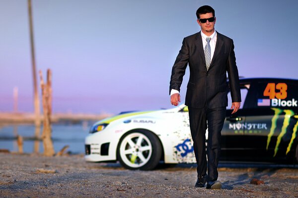 A man in a suit on the shore near a sports car