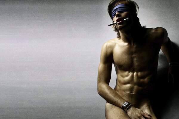 A man against the wall with a naked torso and a blindfold. A handsome man with an alluring look, a slight unshaven face