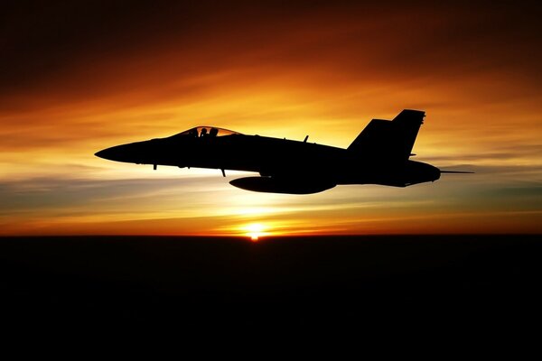 Un avión militar vuela en medio de una puesta de sol
