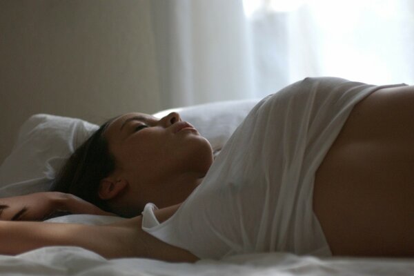 A girl in a transparent white T-shirt is sleeping on the bed