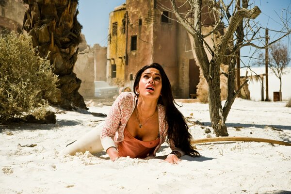 Megan Fox est allongée sur le sable au milieu des ruines de la ville et regarde vers le haut avec peur