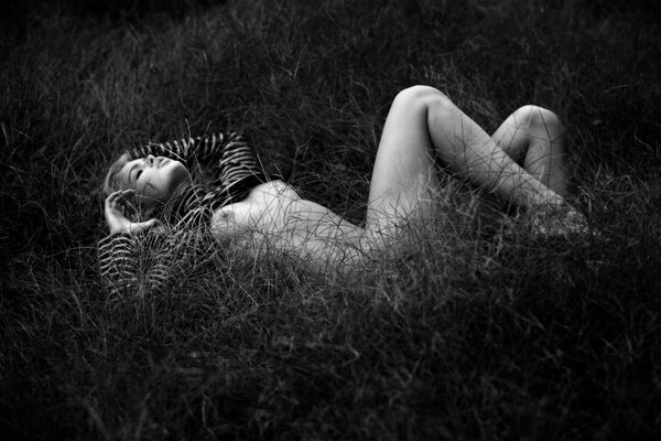 Black and white photo of a naked girl lying in the grass