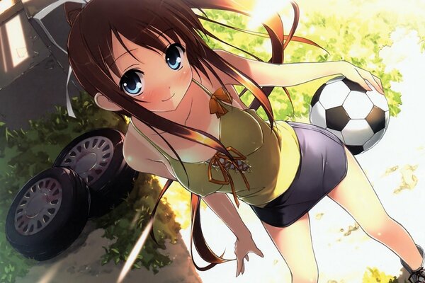 A girl with big eyes in a green lane on the background of wheels and grass with a soccer ball in her hands