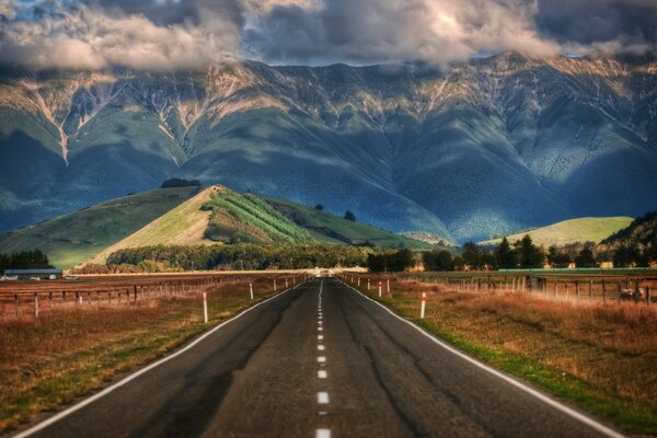 Die Straße ist von Feldern mit Blick auf die Hügel und Berge Neuseelands umgeben
