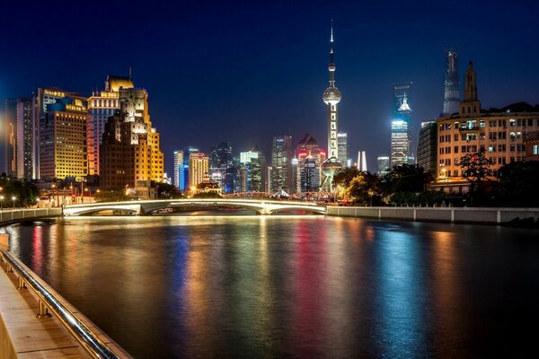 Die Wolkenkratzer von Shanghai leuchten in der Nacht mit Lichtern und spiegeln sich im Fluss wider