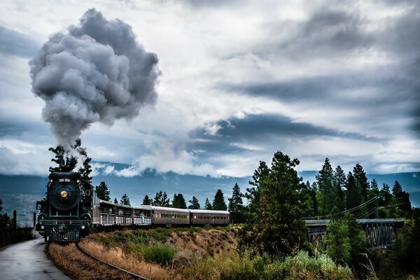 El ferrocarril en el borde de un acantilado en una zona boscosa y una gran composición de vagones arrastra una locomotora de vapor