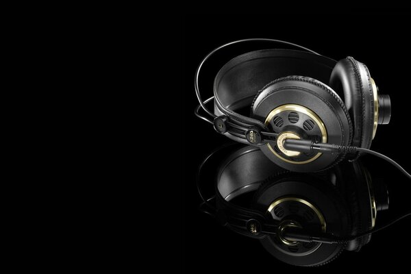 Black and gold headphones are reflected in the black surface