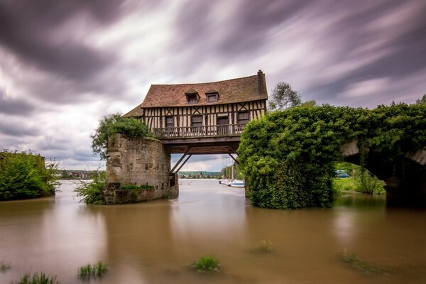 Ein Häuschen hängt an einer kaputten Brücke über dem Wasser