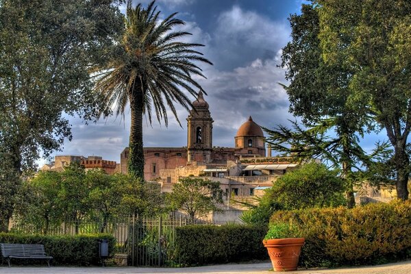 Panchina, recinzione vivente, alberi sullo sfondo della Chiesa