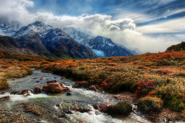 Die Wolken fallen auf die Berge. Landschaft mit Bergblumen und Fluss