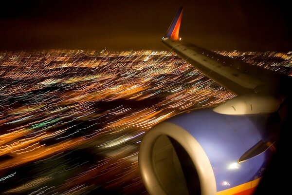 Blick vom Bullaugen auf den Flugzeugflügel und die Lichter der Stadt