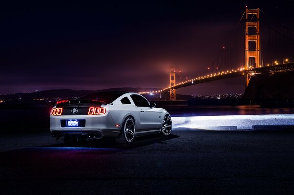Ford Mustang blanco en la noche, iluminando el camino del puente con faros, vista trasera