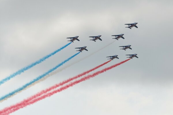 The plane in the sky is releasing blue red and white smoke