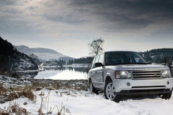 Белый land rover в зимнем пейзаже около озера