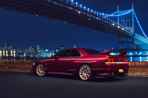 Un auto nissan rossa si trova sotto il ponte di New York di notte
